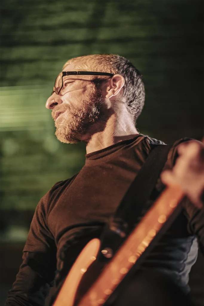 Le bassiste de Giac Taylor, lunettes et barbe, dans une lumière verte, concert à Forest. Photo Didier Vaneesbeck