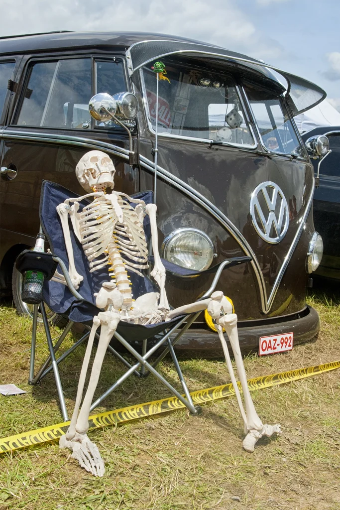 Squelette assis dans une chaise pliante devant un combi Volkswagen, Hot Rod Custom Show Chimay
