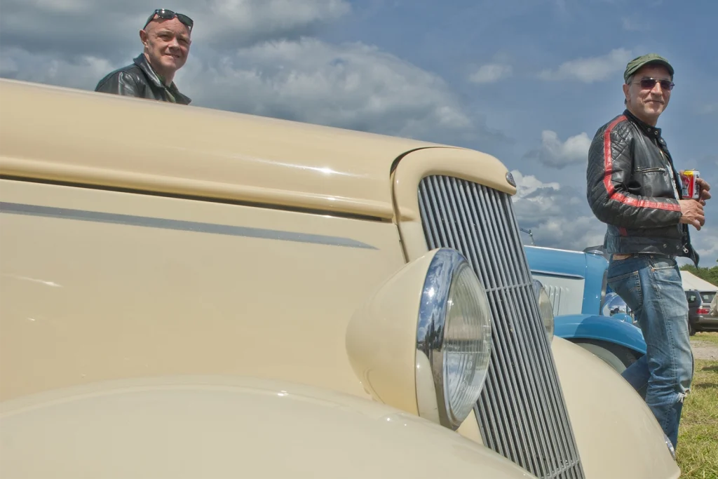 Passionné en blouson de cuir près d'un hot rod crème à calandre chromée, Hot Rod Custom Show Chimay