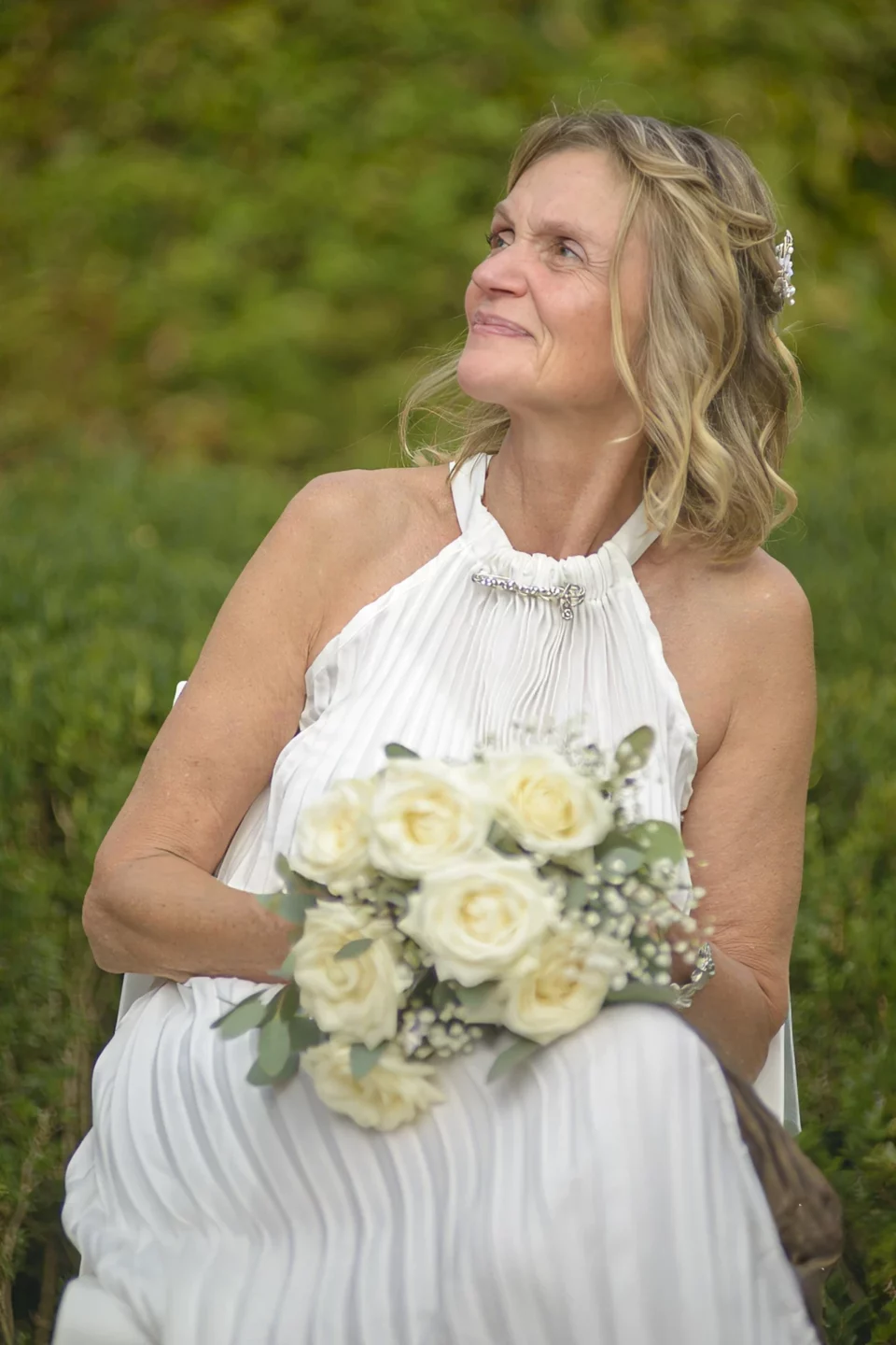 Mariée en robe blanche tenant un bouquet de roses blanches, le regard levé