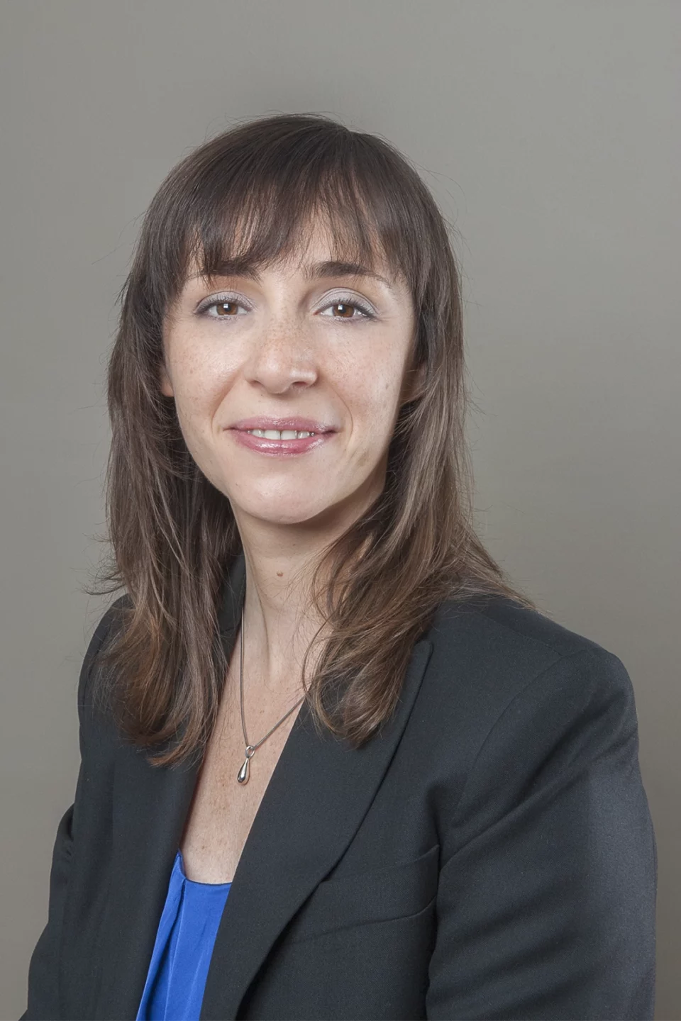Portrait professionnel d'une femme souriante en veste noire sur fond gris