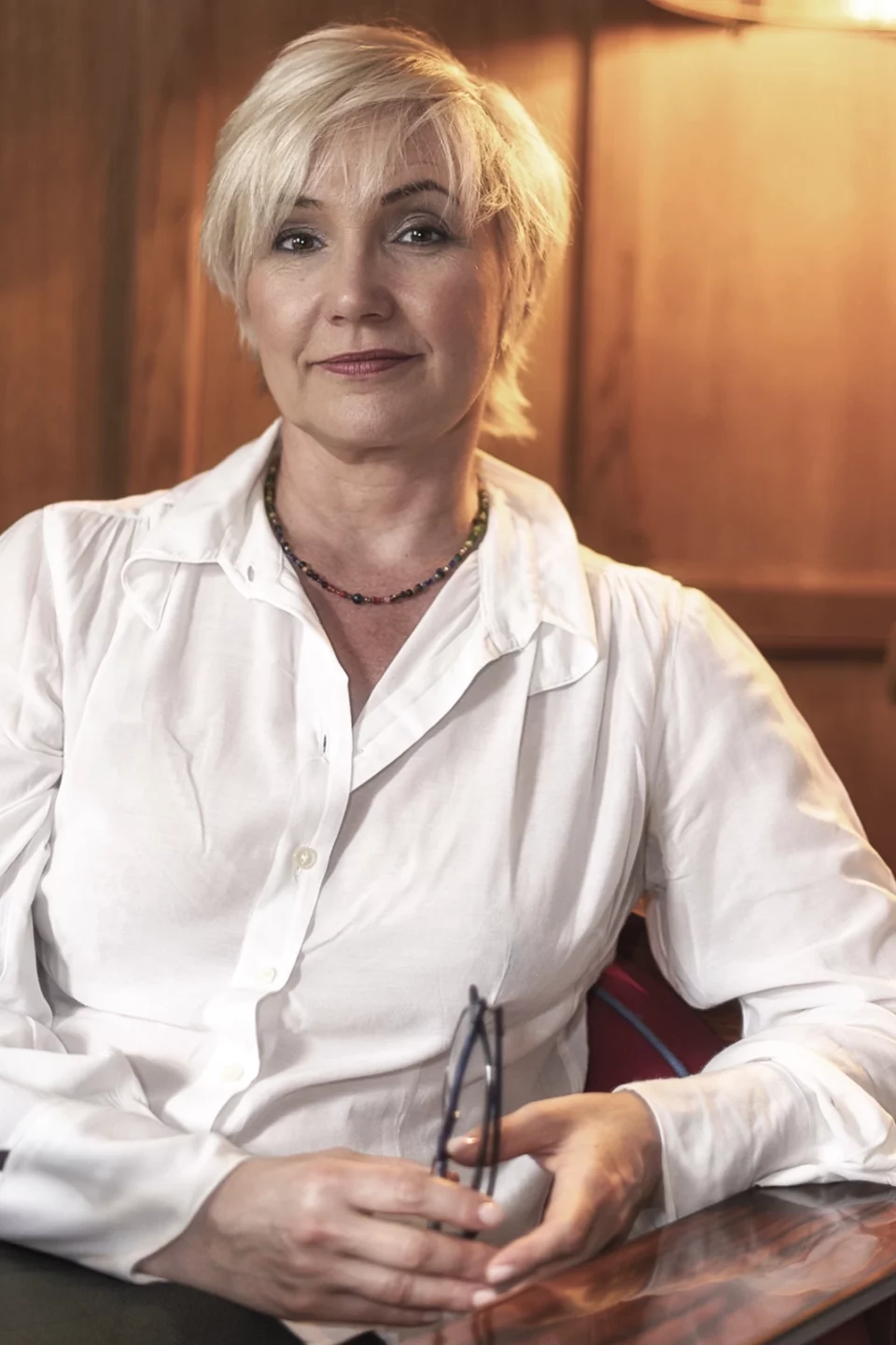 Portrait d'une femme blonde en chemise blanche, assise dans une lumière chaude et boisée
