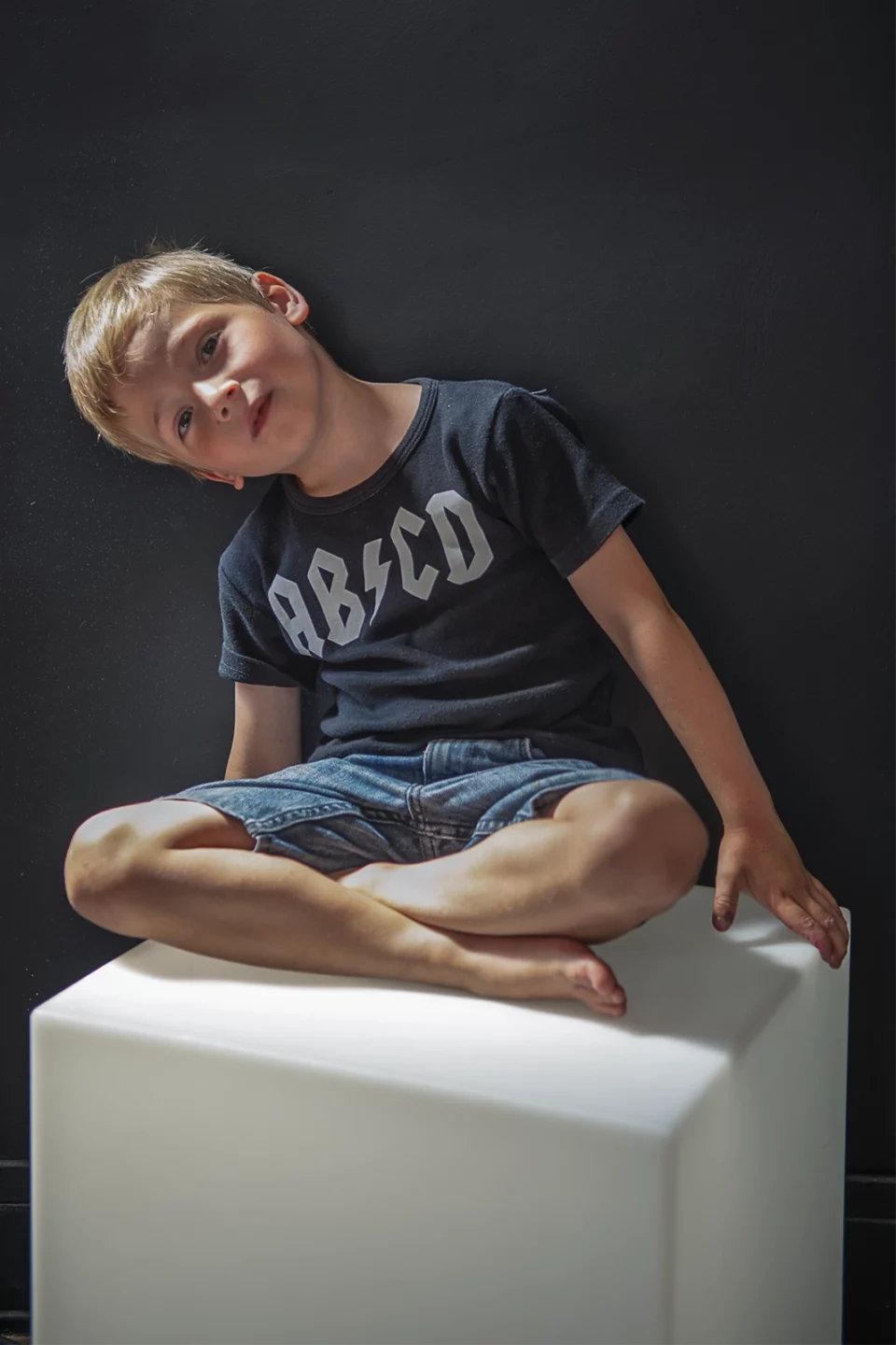 Portrait en studio d'un petit garçon souriant, assis sur un cube blanc