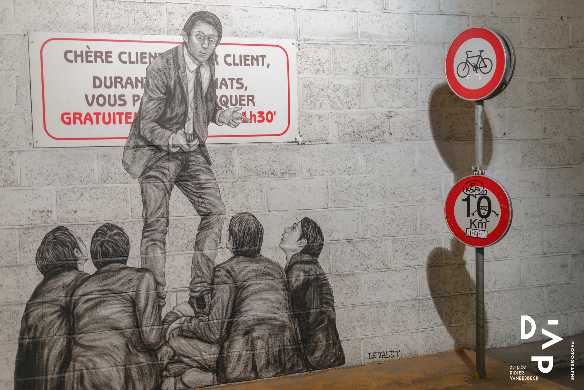 Fresque en noir et blanc d'un homme debout sur des enfants, entre deux panneaux de signalisation – Strokar Inside, Bruxelles 2018