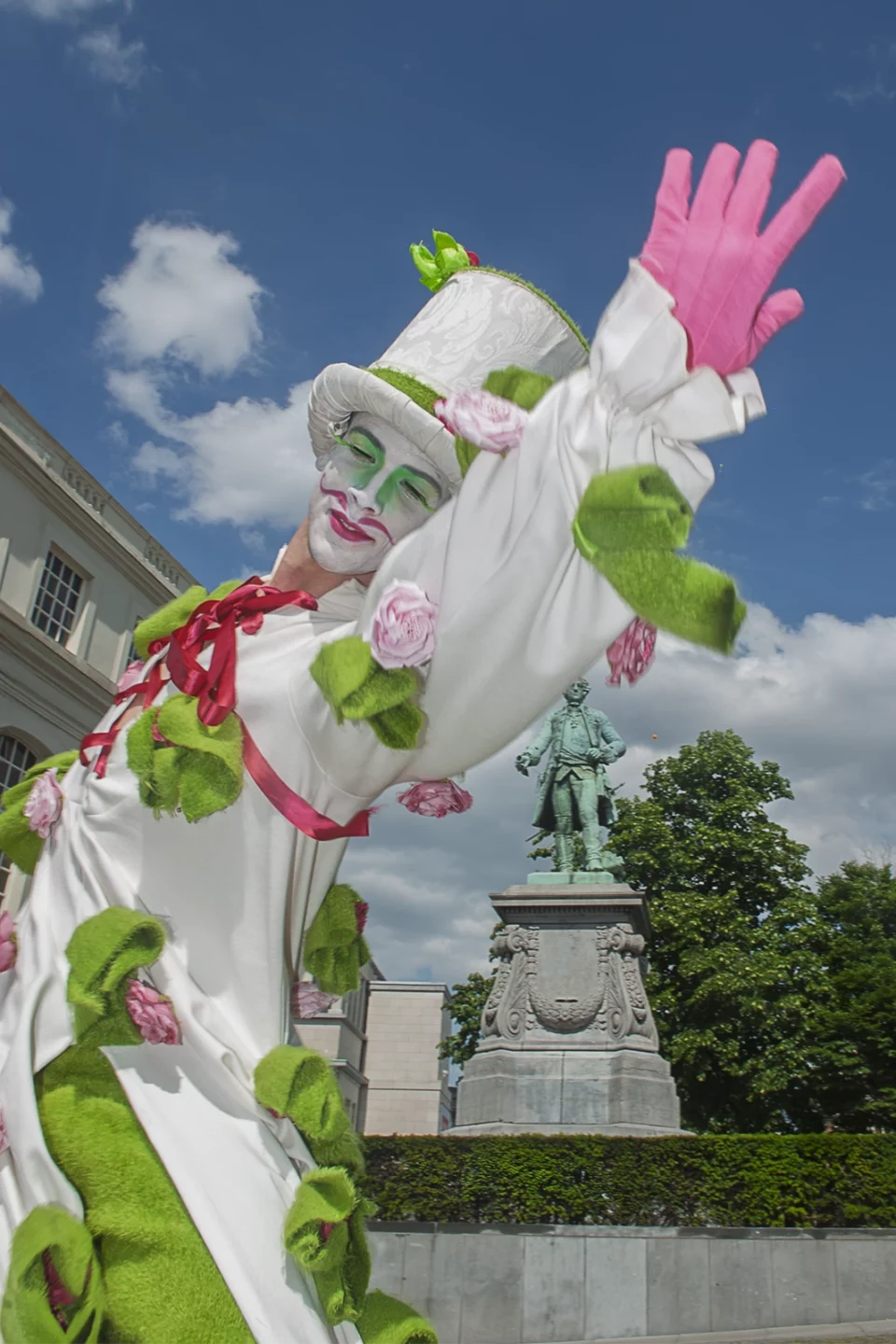 Personnage costumé couvert de fleurs, gant rose levé, lors d'un défilé de rue